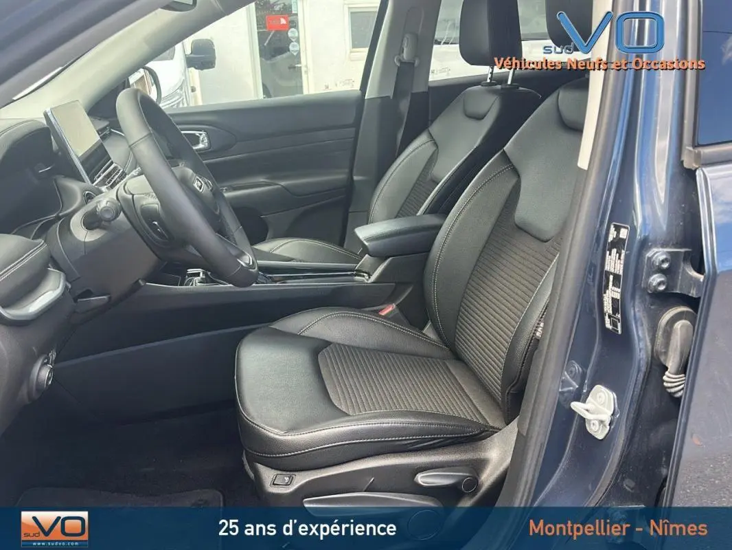 Intérieur avant du Jeep Compass bleu 2023, sièges noirs en cuir avec accoudoir central et tableau de bord moderne visible.