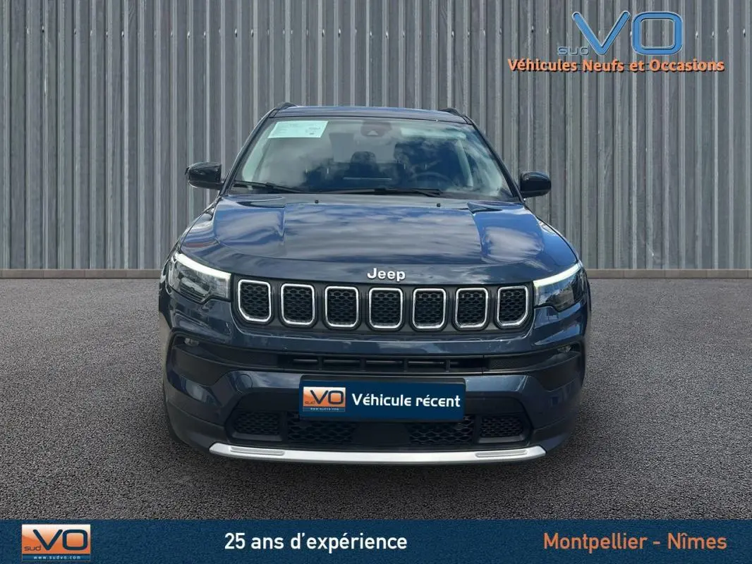 Vue frontale d'un Jeep Compass bleu 2023 avec calandre distinctive et phares LED allumés sur fond neutre.