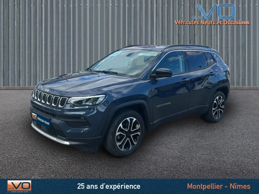 Jeep Compass bleu en 3/4 avant droit, avec barres de toit et jantes 18 pouces visibles sur fond urbain.