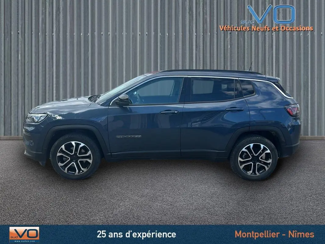 Profil côté gauche d'un Jeep Compass bleu 2023 avec jantes 18 pouces, barres de toit et vitres teintées.