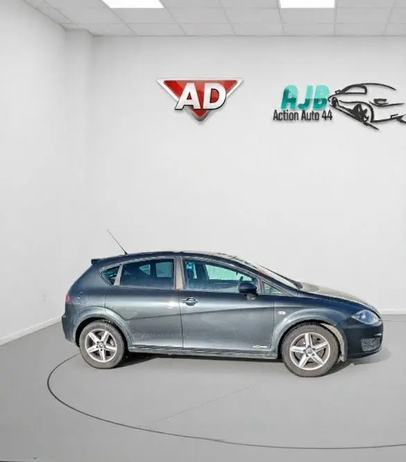 Vue de profil côté gauche d'une SEAT LEON II noire de 2013 avec jantes alu 16 pouces dans un showroom blanc.