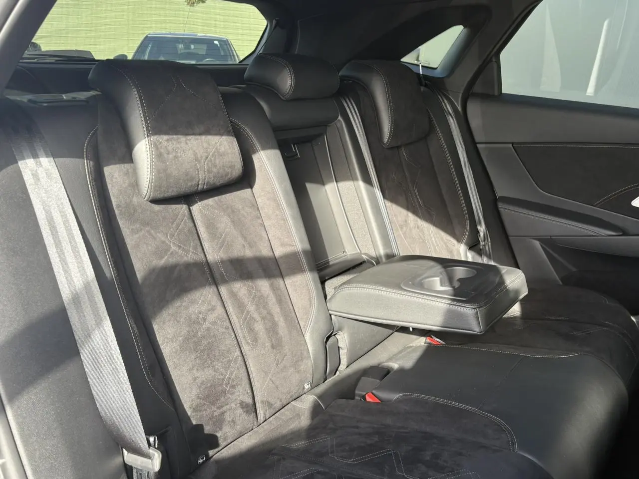 Vue intérieure arrière du DS7 2024 en Alcantara noir profond avec accoudoir central déployé et surpiqûres Carmin et Or.
