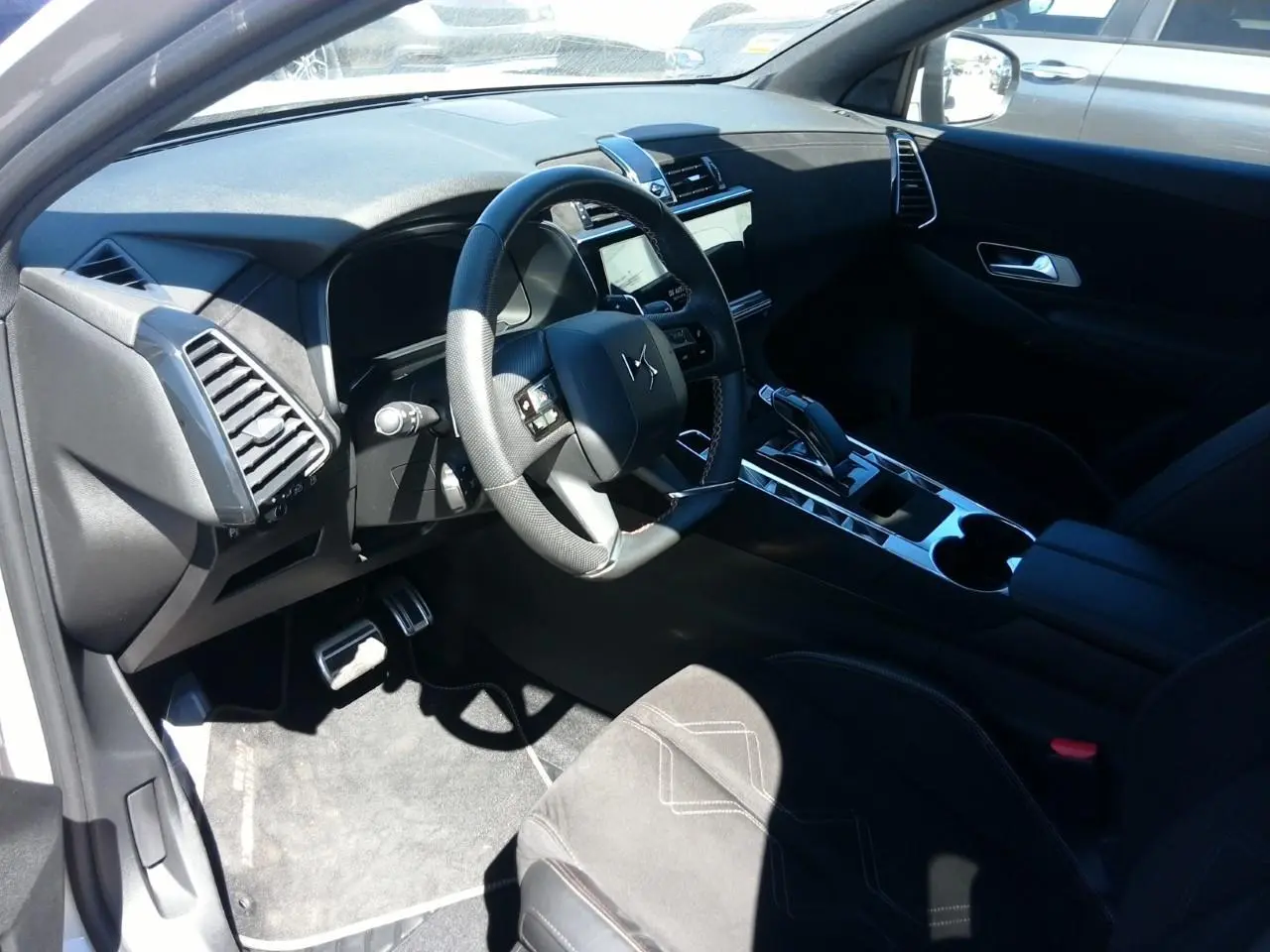 Vue intérieure côté conducteur du DS7 2024, volant cuir noir, console centrale brillante et sellerie Alcantara noire.