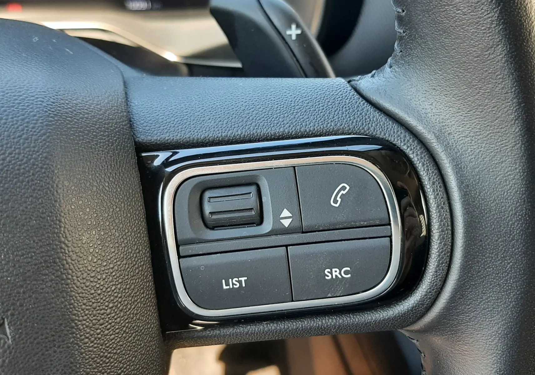 Gros plan sur les commandes gauche du volant en cuir noir du Citroën C5 Aircross Hybrid 2024, boutons multifonctions visibles.