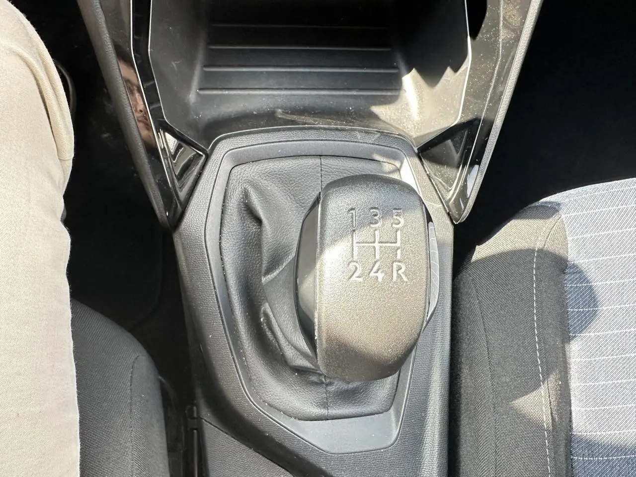 Gros plan sur le levier de vitesses manuel noir de la Peugeot 208 blanche, avec siège conducteur partiellement visible.
