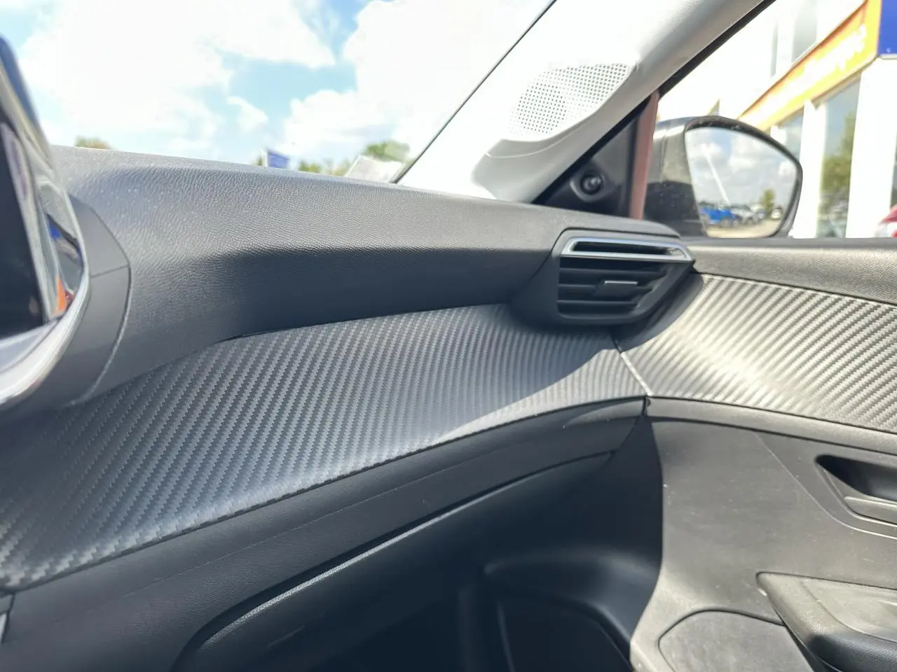 Détail de la garniture intérieure côté passager de la Peugeot 208 1.2i PT 75 blanche, avec effet carbone.