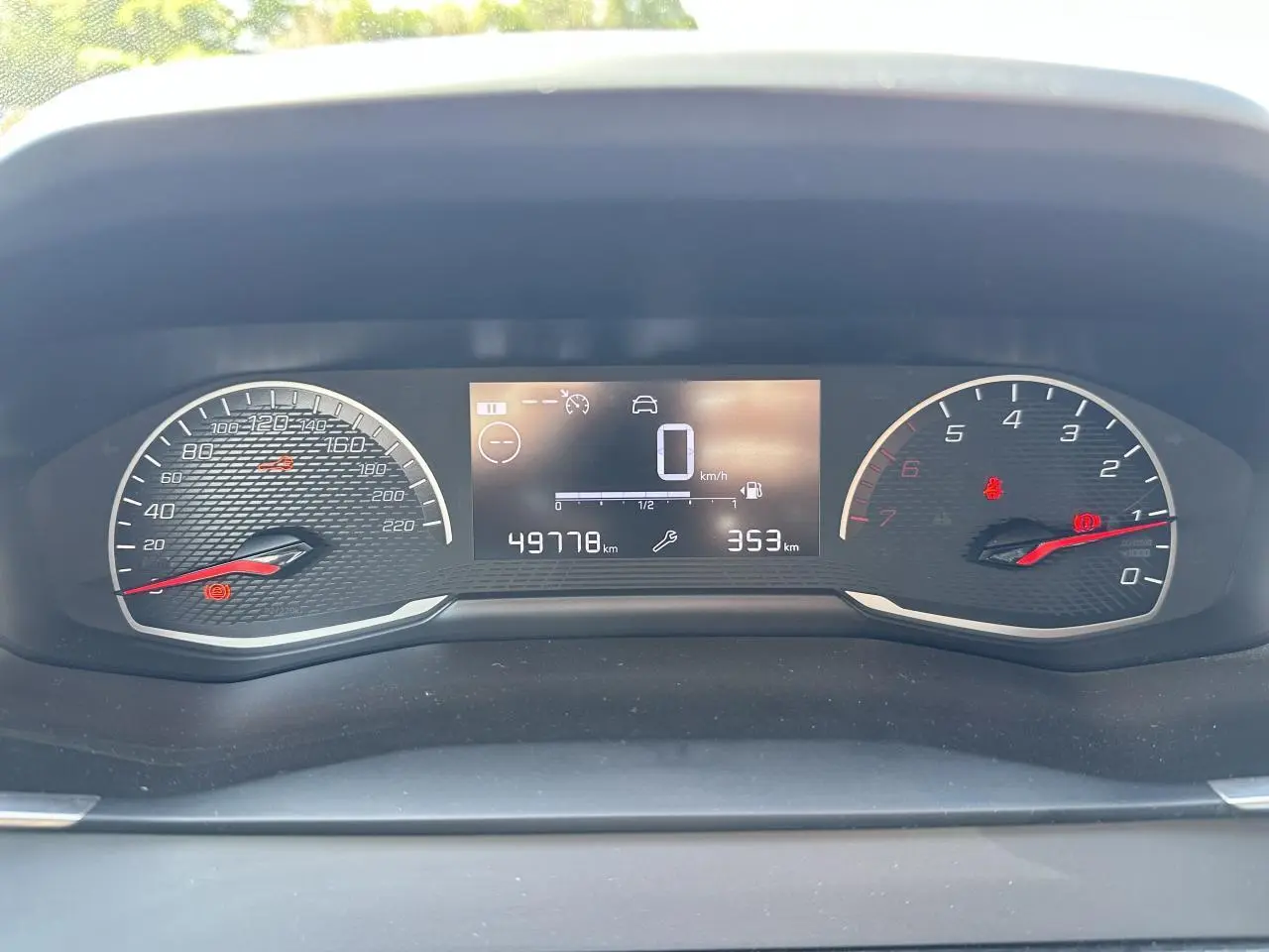 Vue rapprochée du tableau de bord numérique du Peugeot 208 blanc, affichant la vitesse à zéro et le compteur kilométrique.