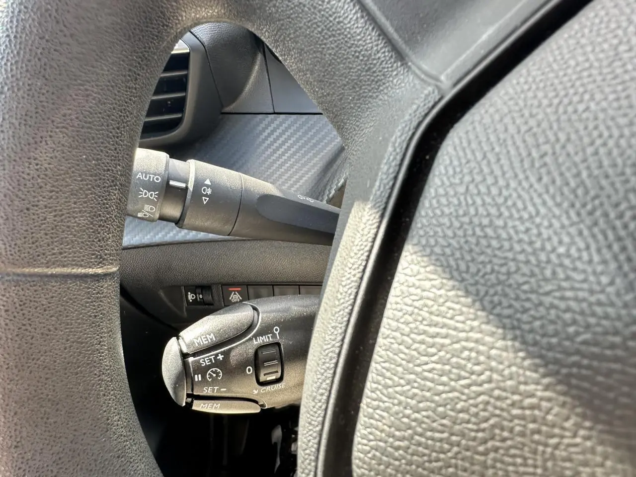 Gros plan sur la commande de régulateur de vitesse à gauche du volant d’une Peugeot 208 blanche, intérieur noir.