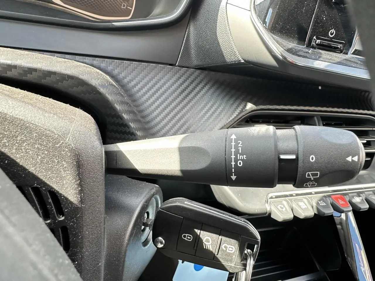 Gros plan sur la commande d’essuie-glace et la clé insérée dans le contact d’un Peugeot 208 blanc, intérieur avec finition carbone.