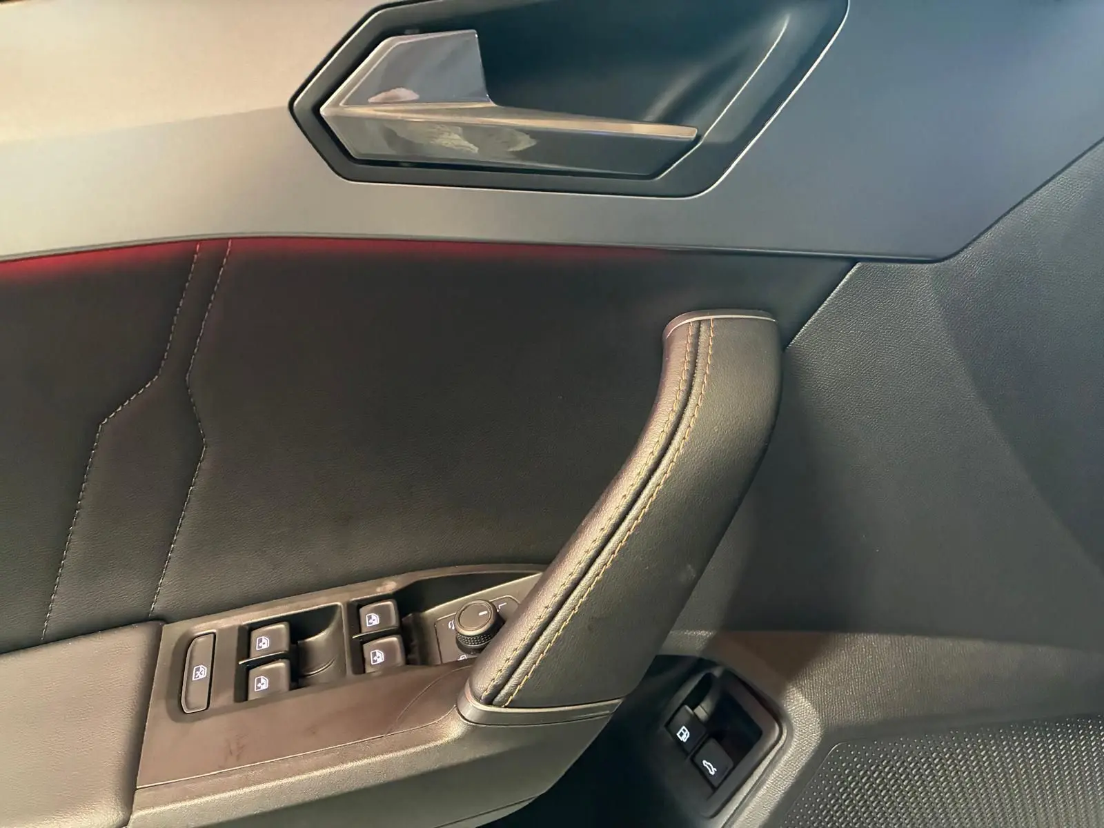 Vue intérieure du panneau de porte côté gauche d'une CUPRA Formentor 1.4 E-HYBRID 2024 avec commandes de vitres et poignée en cuir noir.