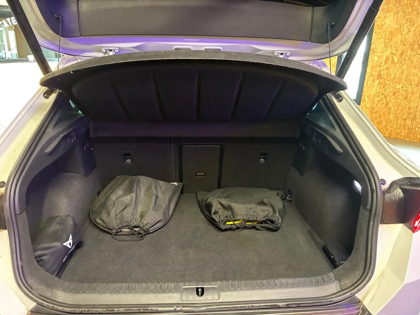 Coffre ouvert d’une CUPRA Formentor gris 2024, vue arrière, montrant un espace de chargement avec deux sacs noirs.