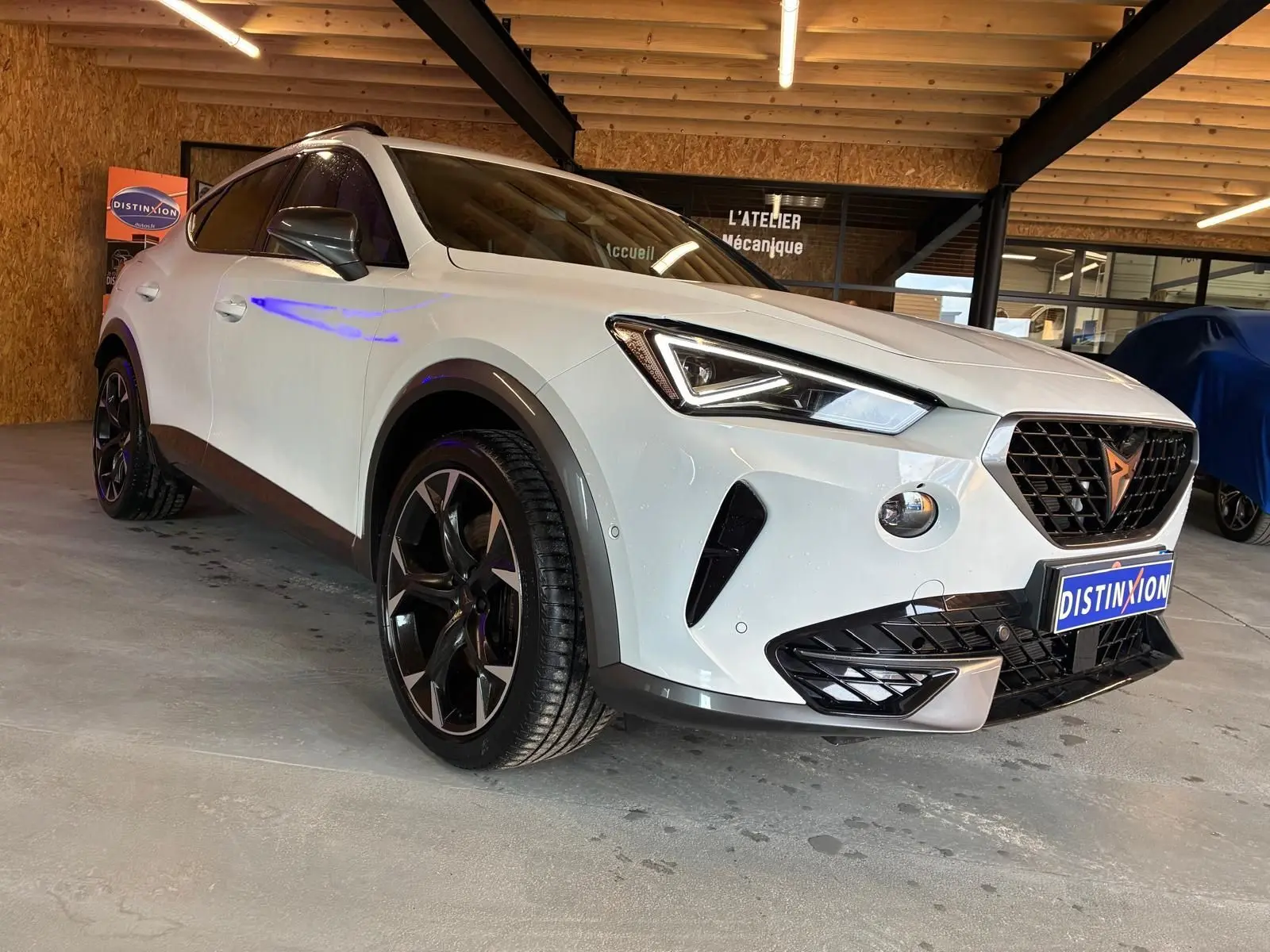 Vue 3/4 avant d'une CUPRA Formentor gris clair 2024, avec calandre noire et jantes noires distinctives.