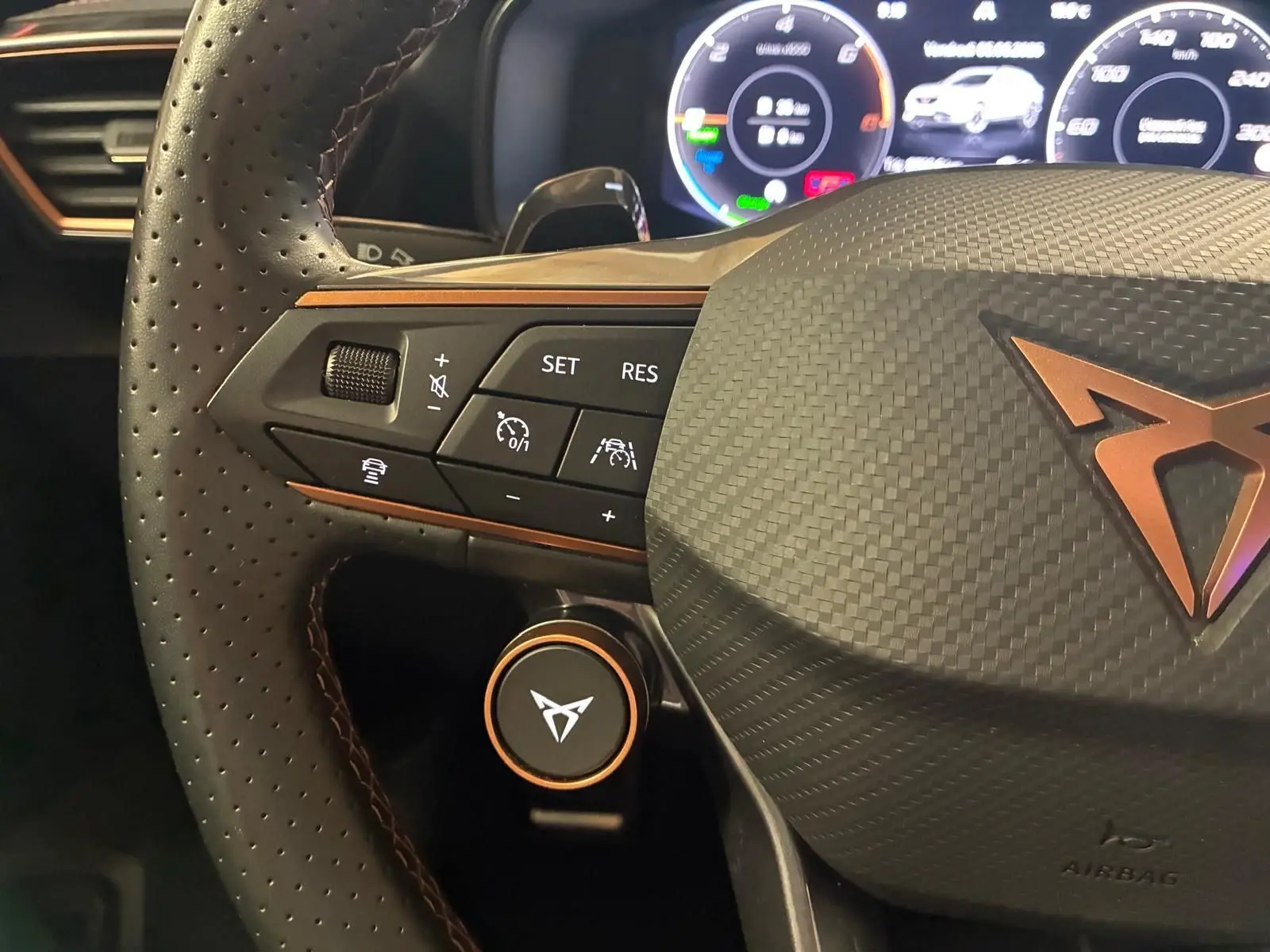 Gros plan sur le volant perforé gris du CUPRA Formentor 1.4 E-HYBRID 2024 avec commandes intégrées et logo cuivré.