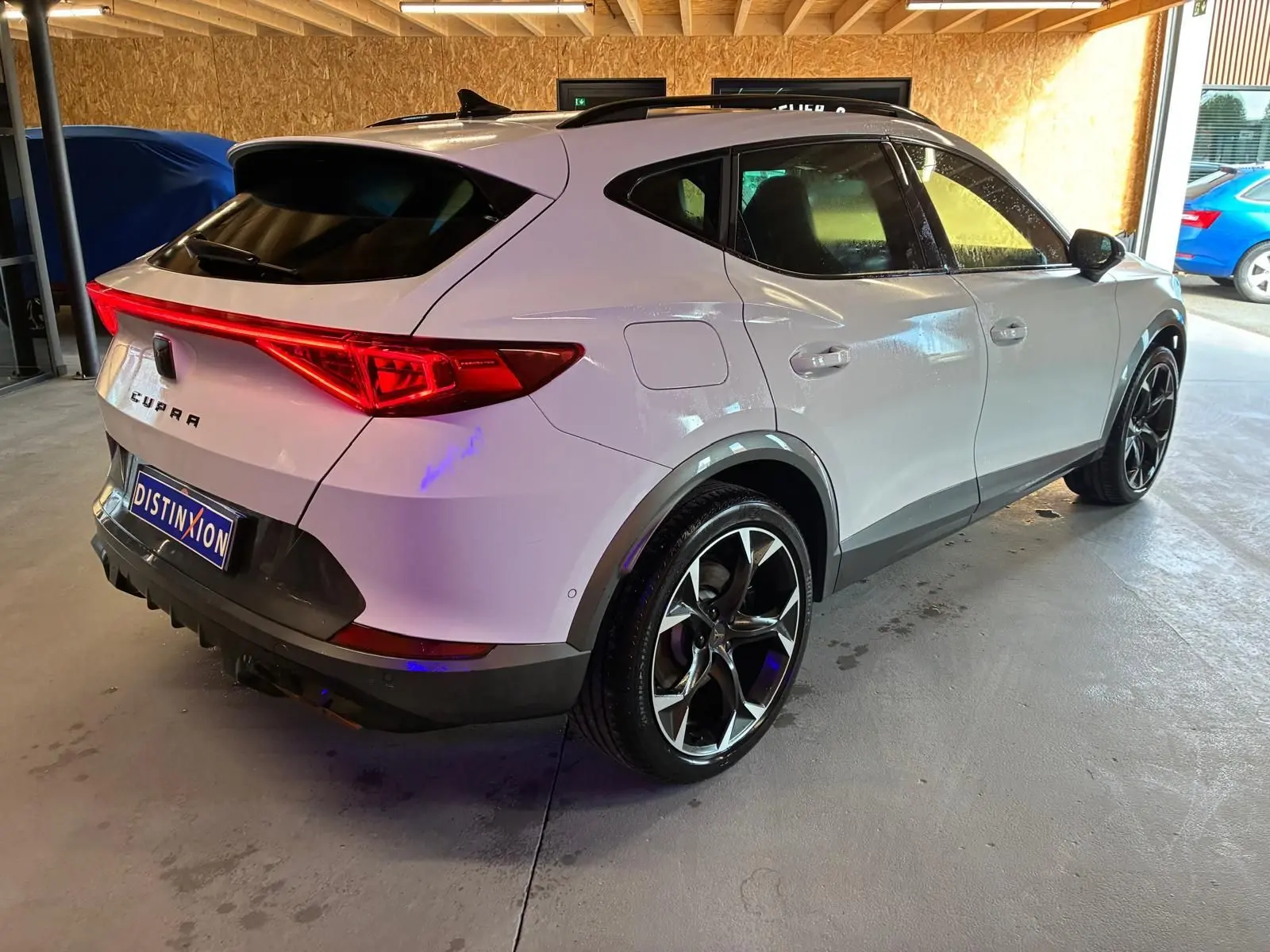 Vue 3/4 arrière droit d'un CUPRA Formentor gris avec feux arrière allumés et jantes noires bicolores.