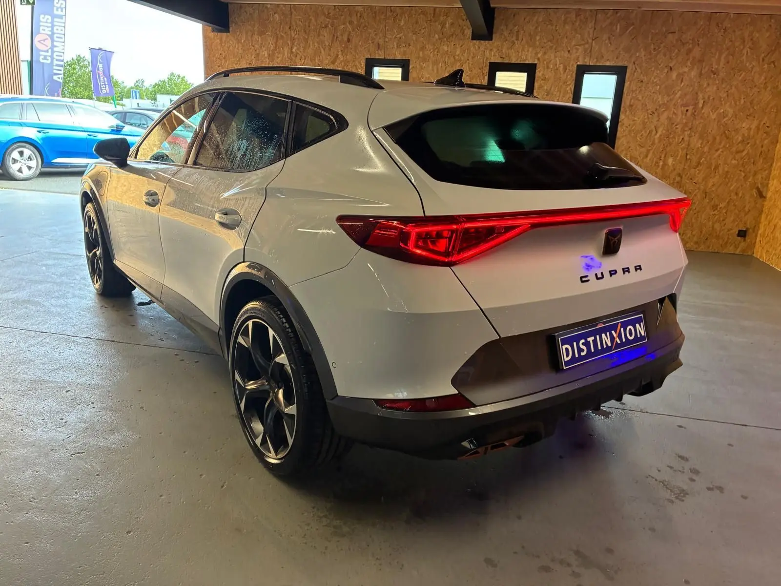 Vue 3/4 arrière droite d'une CUPRA Formentor gris métallisé avec feux arrière allumés dans un garage.