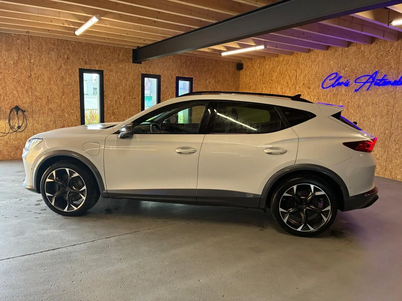 Vue de profil côté gauche du CUPRA Formentor gris clair 2024 en hybride rechargeable, avec jantes noires et toit noir dans un garage.