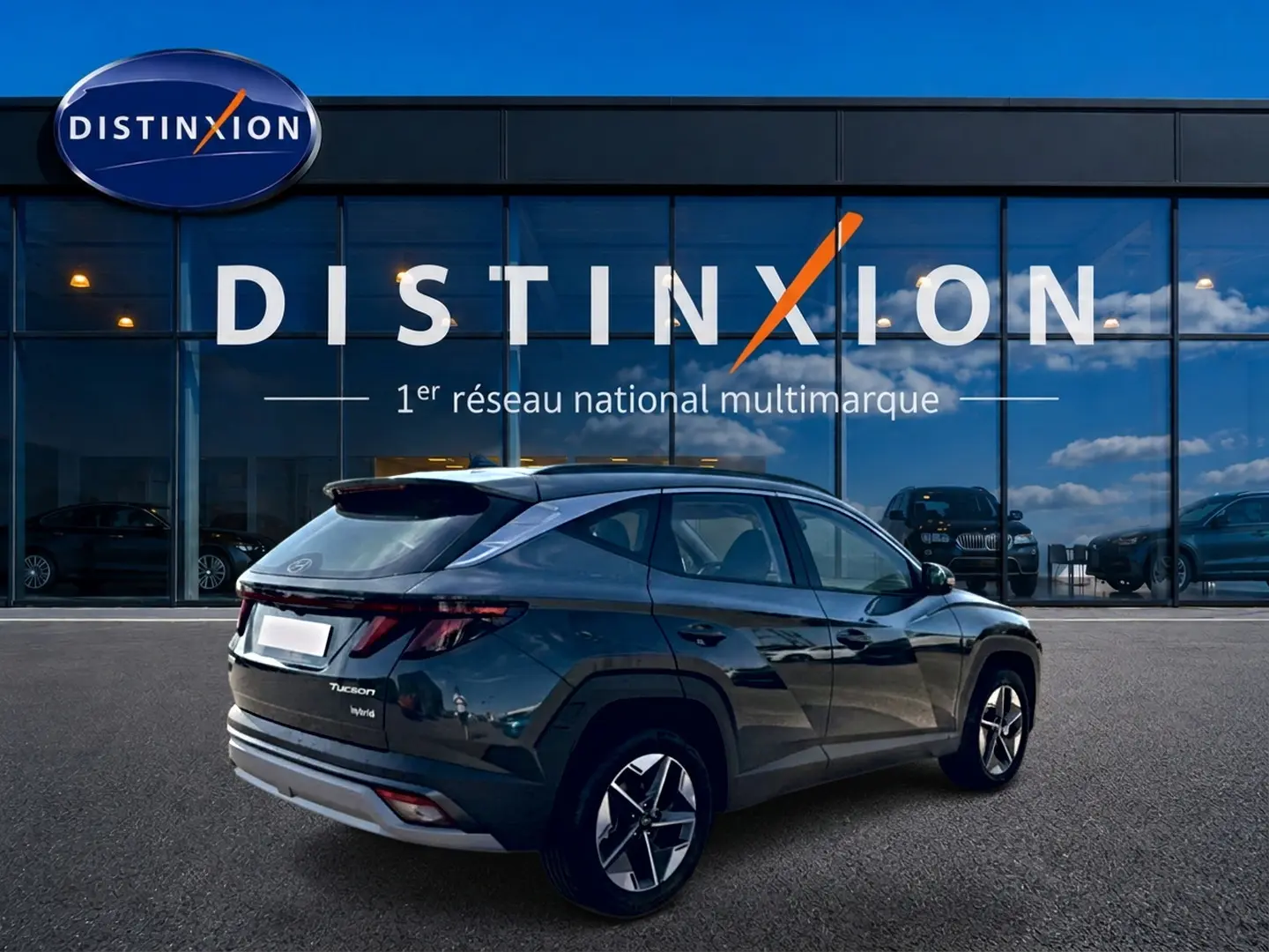 Vue 3/4 arrière droite d'un Hyundai Tucson hybride vert devant une vitrine Distinxion avec jantes alu 18 pouces.