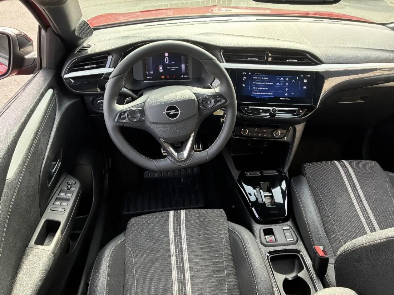 Vue intérieure avant de l’Opel Corsa 1,2 Hybrid 2025, avec volant multifonction, écran tactile et sièges noirs à bandes grises.