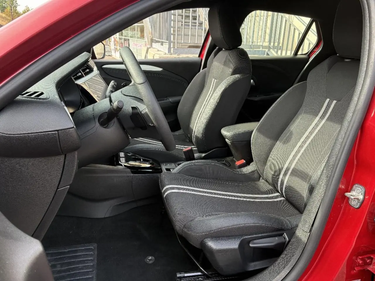 Intérieur avant de l’Opel Corsa 2025 rouge peperoncino, vue côté gauche montrant sièges noirs avec surpiqûres claires.