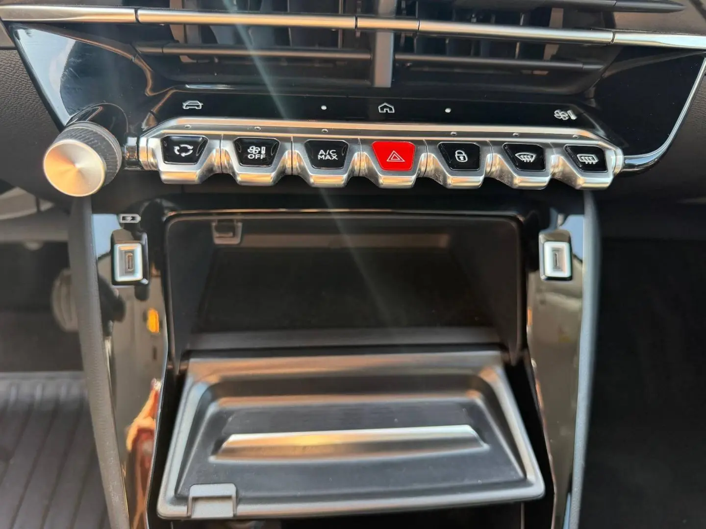 Gros plan sur la console centrale noire brillante de la Peugeot 208 1.2 100ch Allure avec rangements et boutons de commande.