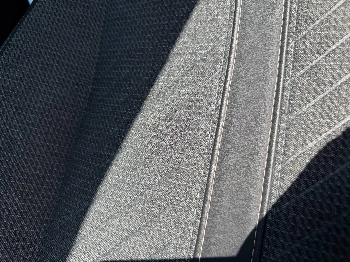 Détail du tissu gris Casual Lomsa avec surpiqûres contrastées sur l'accoudoir central avant du Peugeot 208 2025.