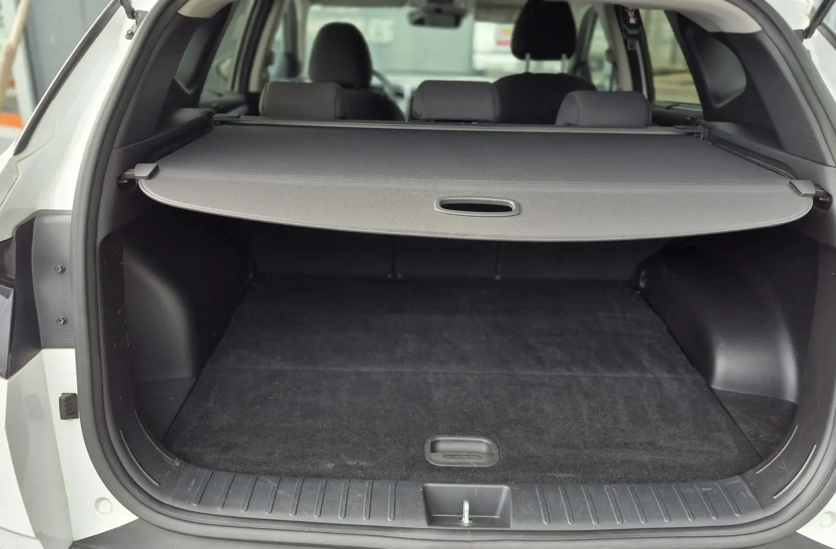 Vue arrière ouverte du coffre noir d’un Hyundai Tucson blanc 2022, avec cache-bagages déployé.