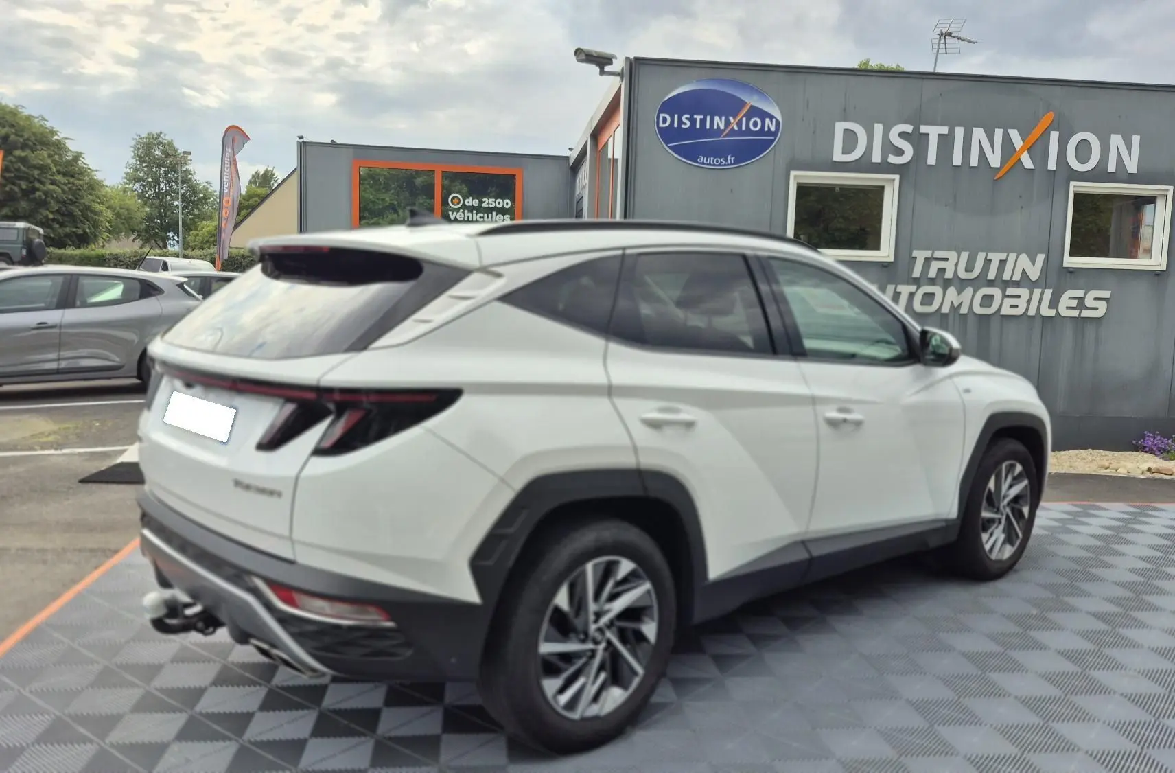 Vue 3/4 arrière droite d’un Hyundai Tucson blanc 2022 avec attelage, stationné devant un concessionnaire Distinxion.