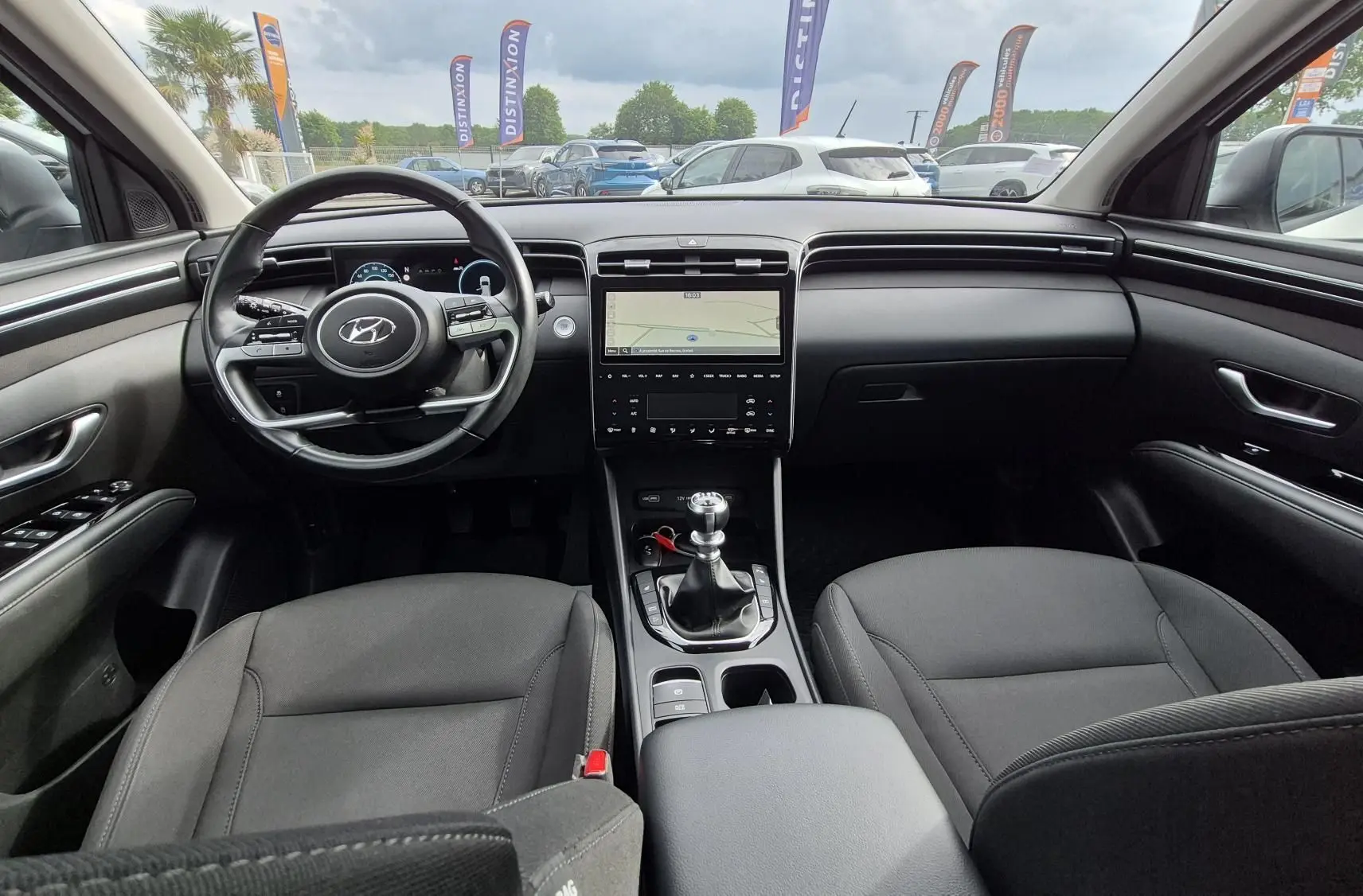 Vue intérieure avant du Hyundai Tucson 2022, montrant le volant, la console centrale avec boîte manuelle et les sièges en tissu noirs.