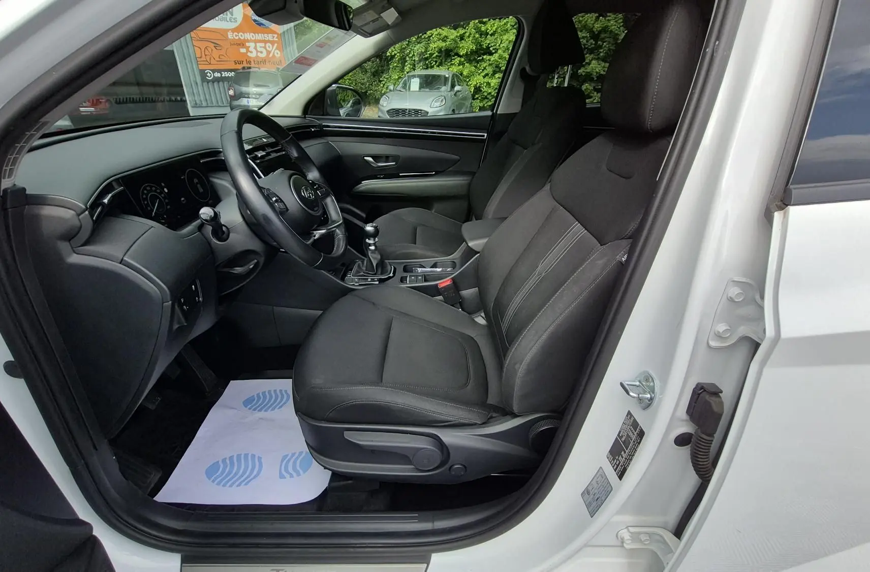 Vue intérieure côté conducteur du Hyundai Tucson blanc 2022, sièges tissu noirs et tableau de bord moderne.