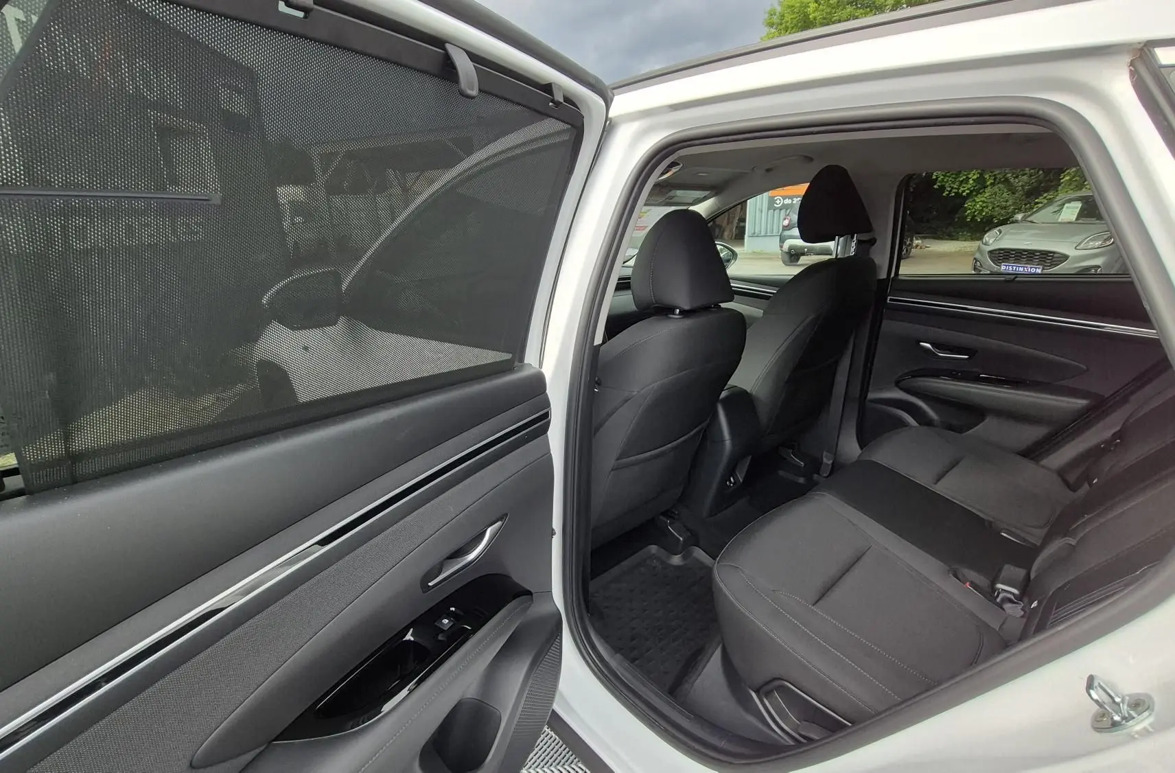 Vue intérieure côté arrière gauche d’un Hyundai Tucson blanc 2022, montrant les sièges arrière en tissu noir et la portière ouverte.