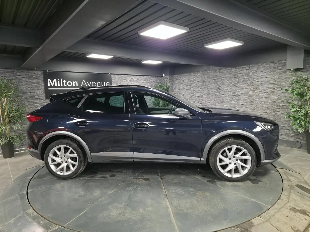 Vue de profil côté gauche du CUPRA Formentor bleu pétrole 2023 avec jantes alliage et toit noir dans un showroom.