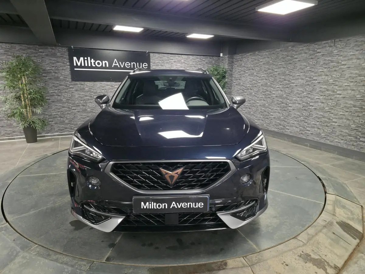 Vue avant d'un CUPRA Formentor bleu pétrole 2023 avec calandre noire et logo cuivre, dans un showroom intérieur.