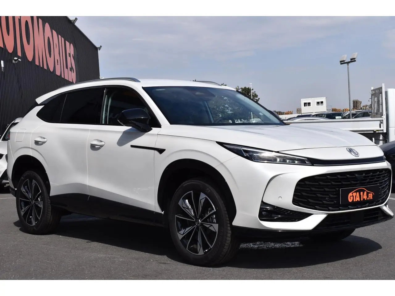 Vue 3/4 avant d’un MG MOTOR EHS blanc 2026, avec calandre noire large et jantes alliage bicolores distinctives.