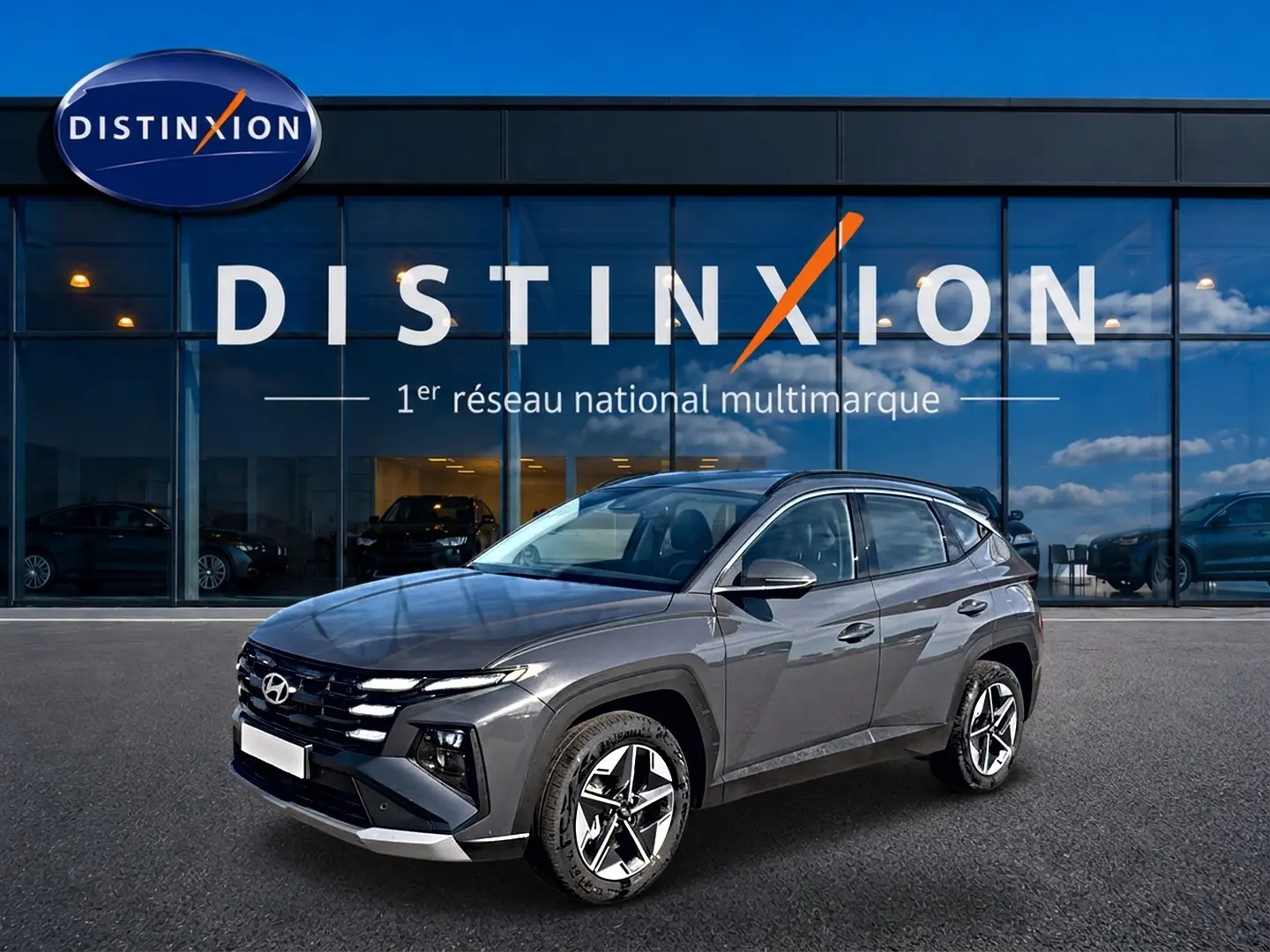 Hyundai Tucson gris ecotonic en 3/4 avant droit, avec jantes alu et calandre distinctive, devant showroom Distinxion.