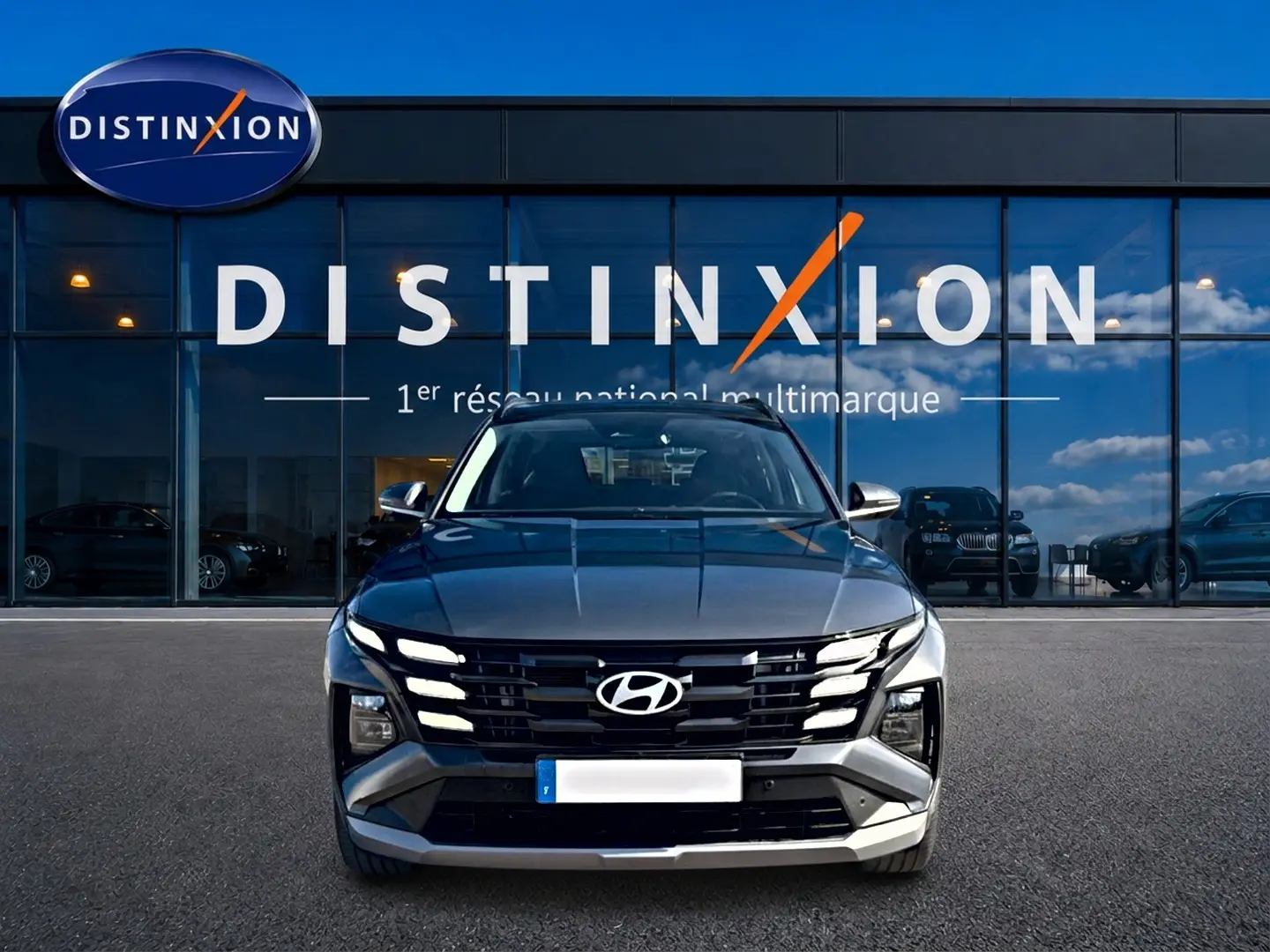Vue avant d'un Hyundai Tucson gris ecotonic 2026 avec calandre noire distinctive et phares LED allumés.