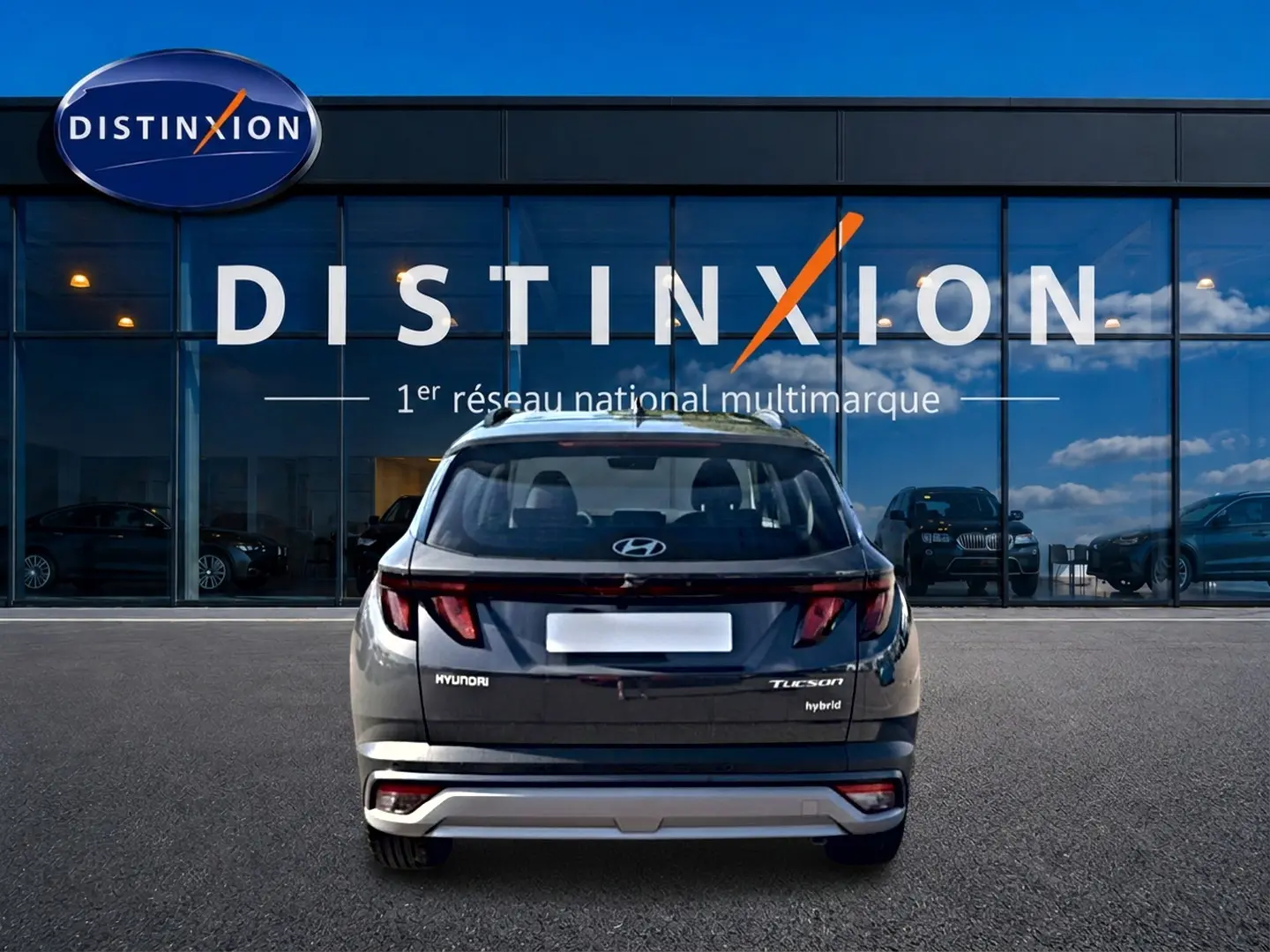 Vue arrière d'un Hyundai Tucson gris ecotonic hybride garé devant une vitrine Distinxion avec reflets de ciel.