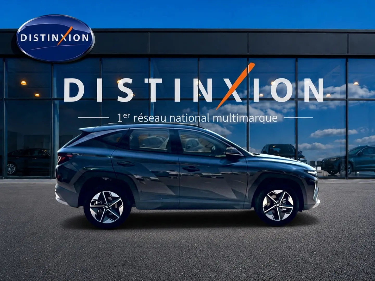 Vue de profil côté gauche d'un Hyundai Tucson gris ecotonic garé devant une vitrine avec logo Distinxion.