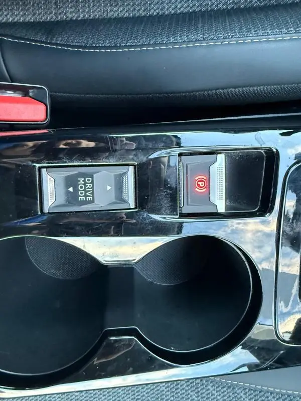 Gros plan sur la console centrale noire du Peugeot 208 Hybrid 110, montrant le bouton Drive Mode et le frein à main électrique allumé.