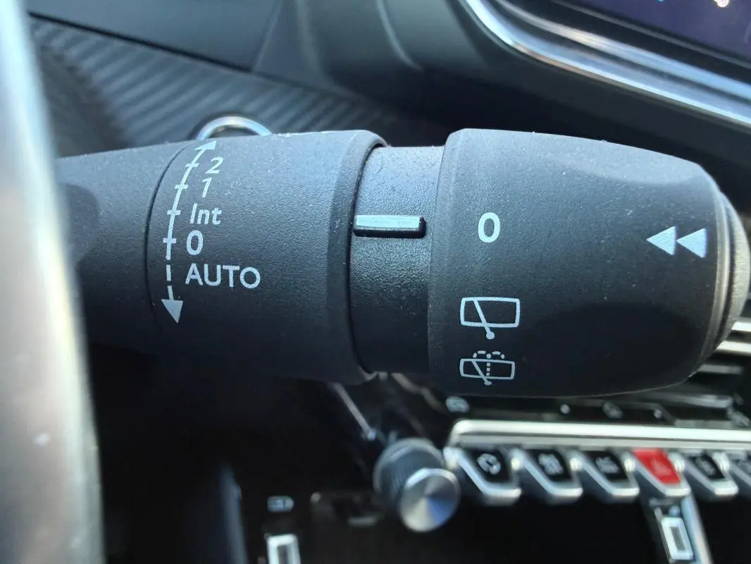 Gros plan sur la commande d’essuie-glace du Peugeot 208 Hybrid 110 e-DCS6 Allure noir, intérieur moderne avec boutons chromés.