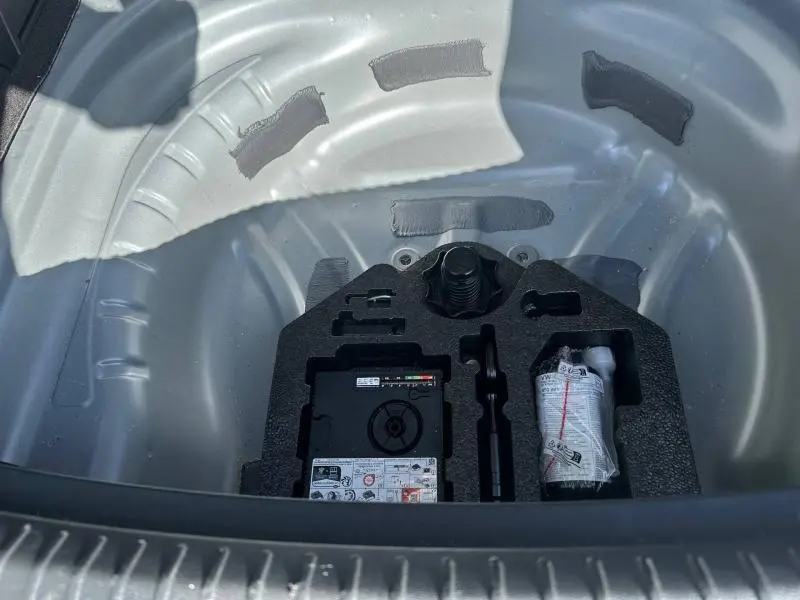 Vue en plongée sur le coffre ouvert d’un SEAT LEON ST 2025 gris, montrant le rangement pour roue de secours et accessoires.