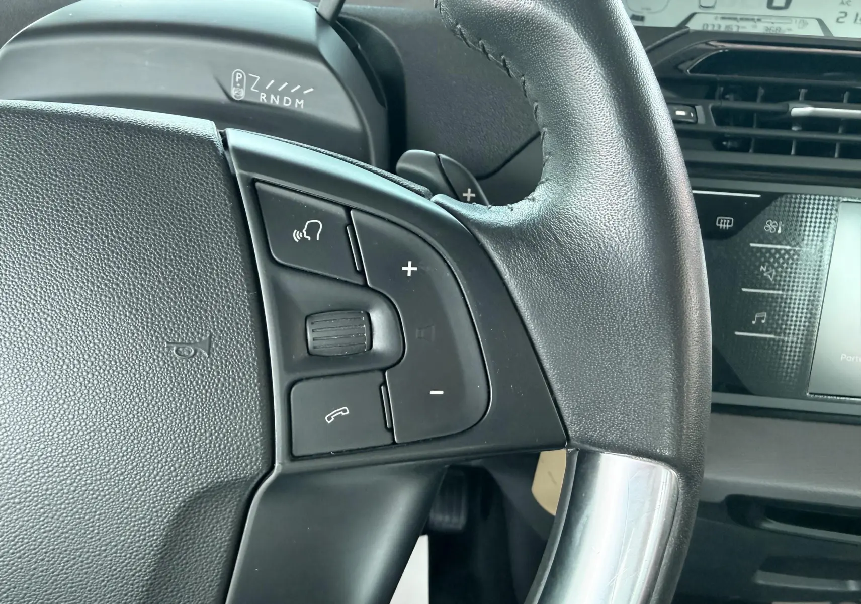 Gros plan sur le volant noir de la Citroën C4 Spacetourer 2019 avec commandes audio et tableau de bord numérique en arrière-plan.