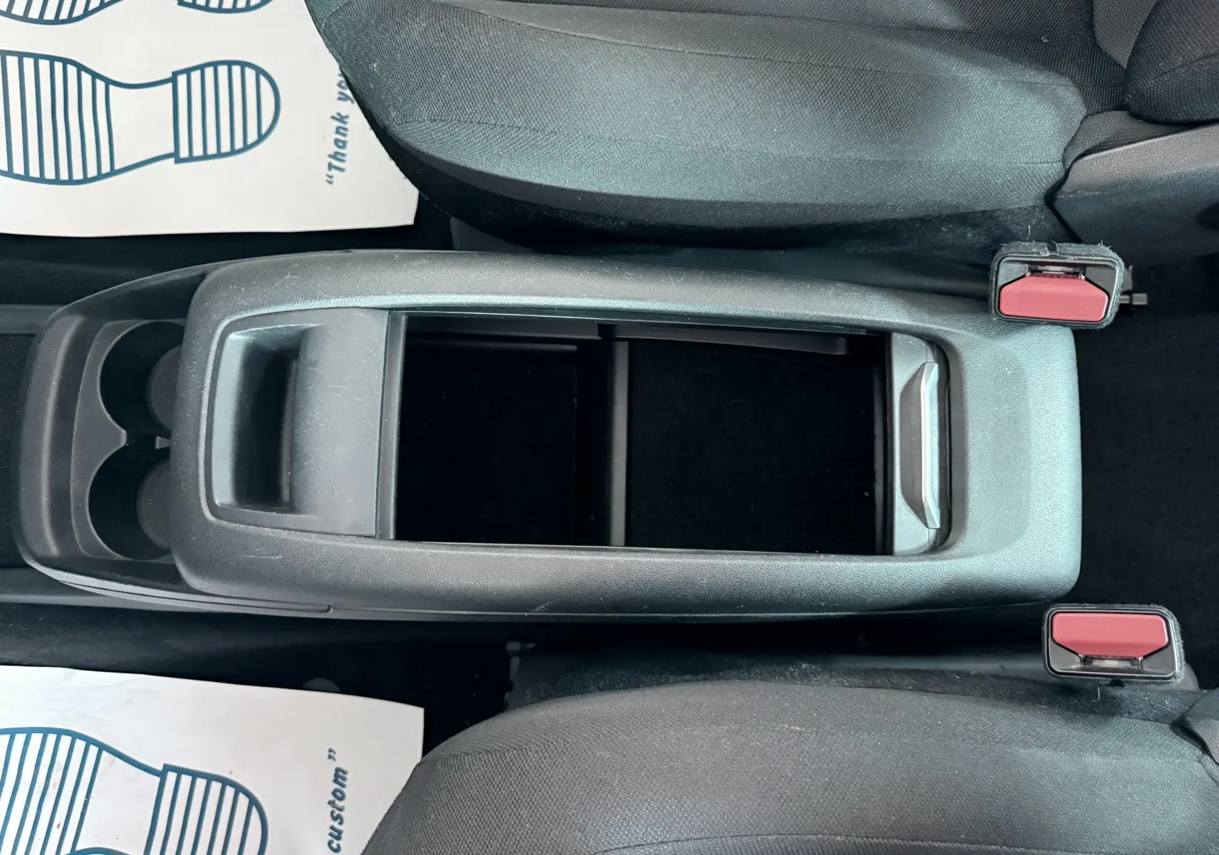Vue plongeante sur la console centrale noire entre les sièges avant en tissu gris foncé du Citroën C4 Spacetourer.