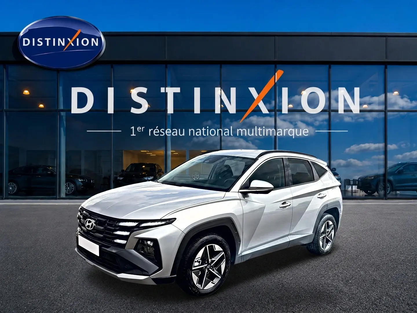 Hyundai Tucson gris shimmering en 3/4 avant droit, avec calandre noire et jantes alliage 18 pouces visibles.