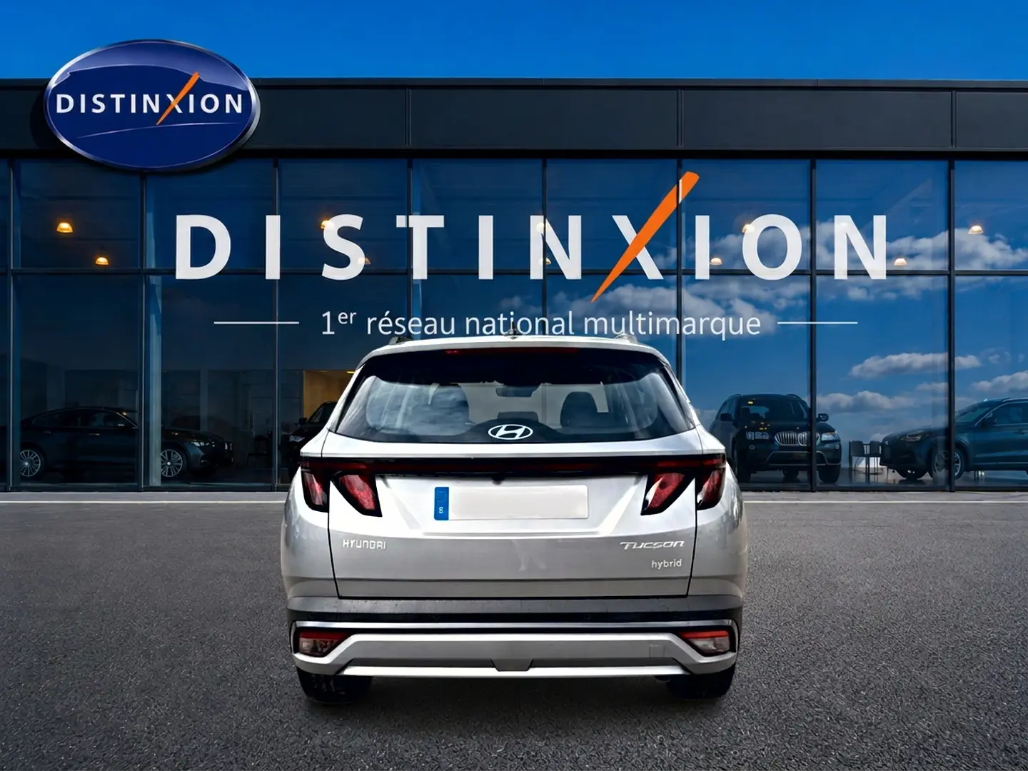 Vue arrière d'un Hyundai Tucson gris shimmering hybride garé devant une vitrine avec logo Distinxion.