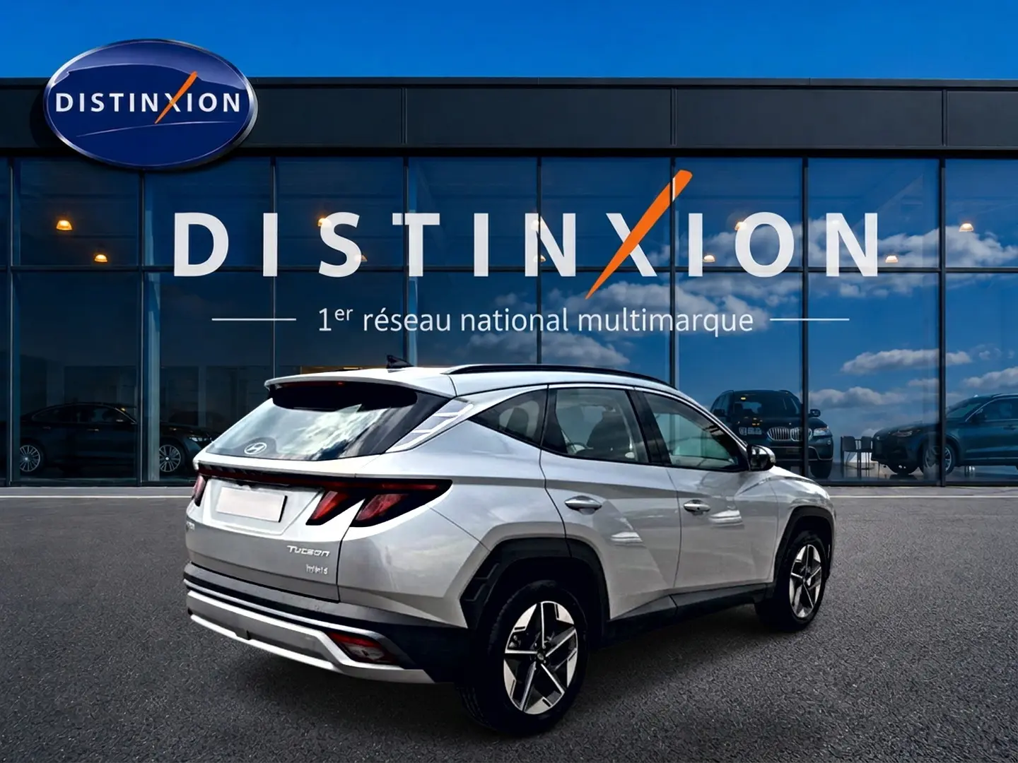 Hyundai Tucson gris shimmering en 3/4 arrière droit, avec feux LED et jantes alliage visibles devant vitrine Distinxion.