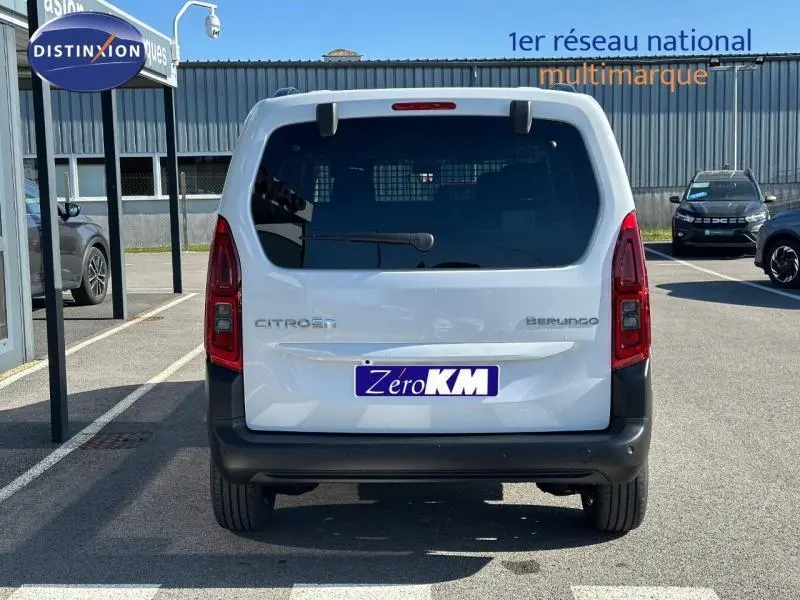 Vue arrière d'un Citroën Berlingo blanc 2025 avec hayon vitré et pare-chocs noir dans un parking extérieur.