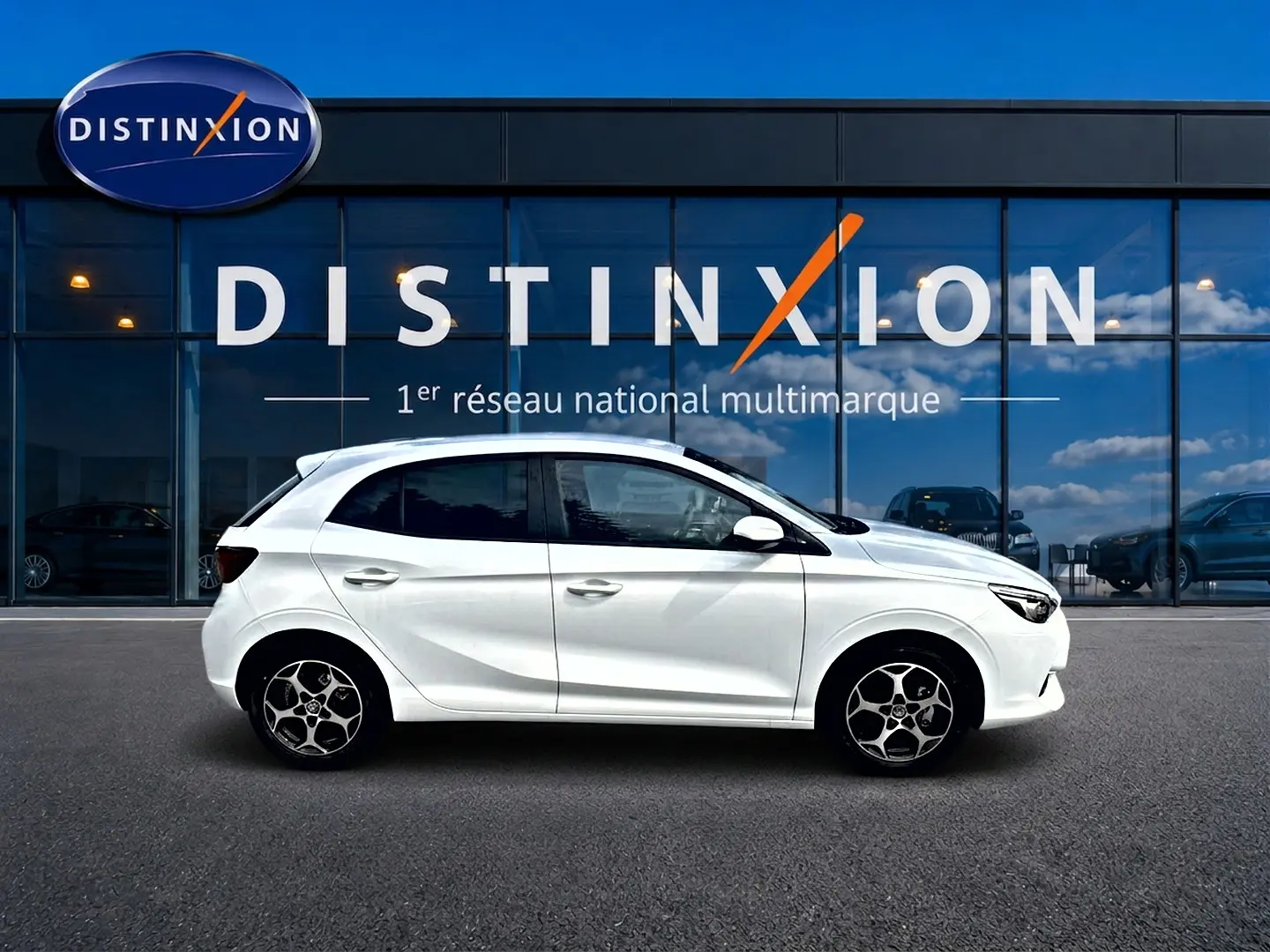 Vue de profil côté gauche d'une MG3 1.5 hybrid 195 luxury blanche avec jantes alu, devant une vitrine Distinxion.