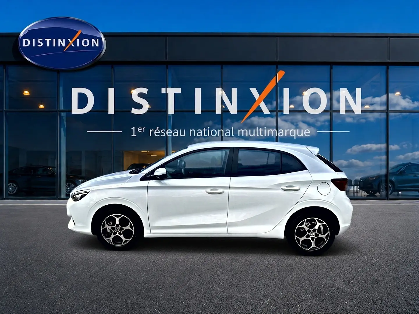 Profil droit d'une MG3 1.5 hybrid 195 luxury blanche, avec jantes alu et vitres teintées, devant une vitrine Distinxion.