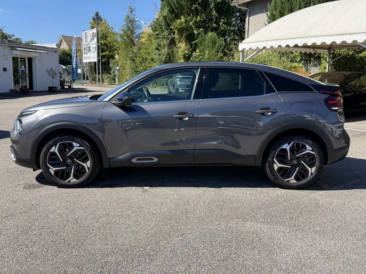 Vue de profil côté gauche d'une Citroën C4 PureTech 130 S&S Shine gris foncé, avec jantes distinctives et toit noir contrasté.