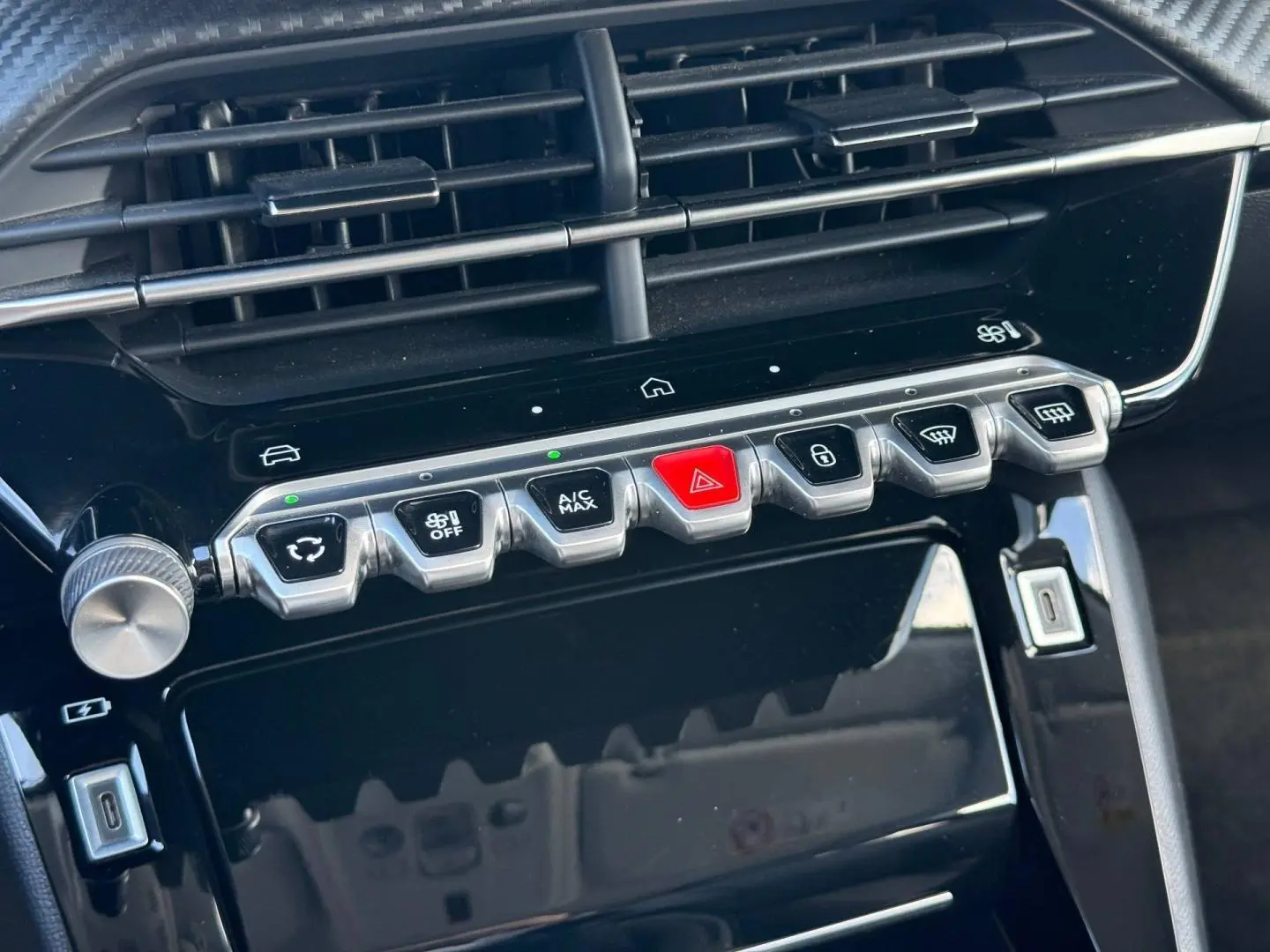 Gros plan sur la console centrale noire brillante du Peugeot 208 1.2 100ch Allure avec boutons argentés et rouge d’alerte.
